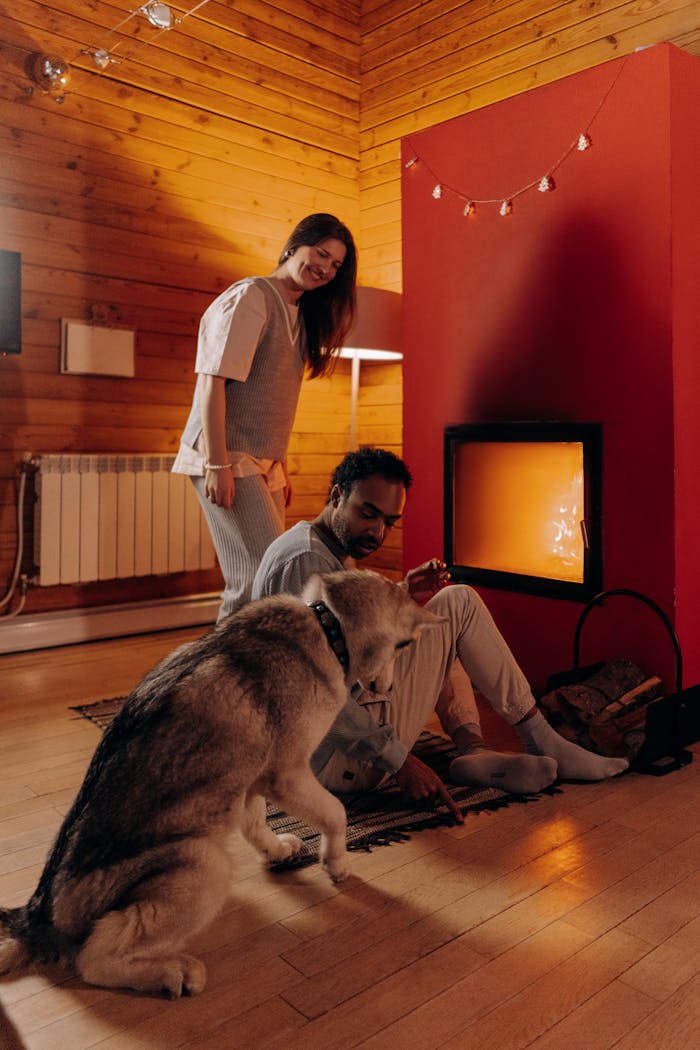 A couple enjoys a warm winter evening indoors with their dog by the fireplace.